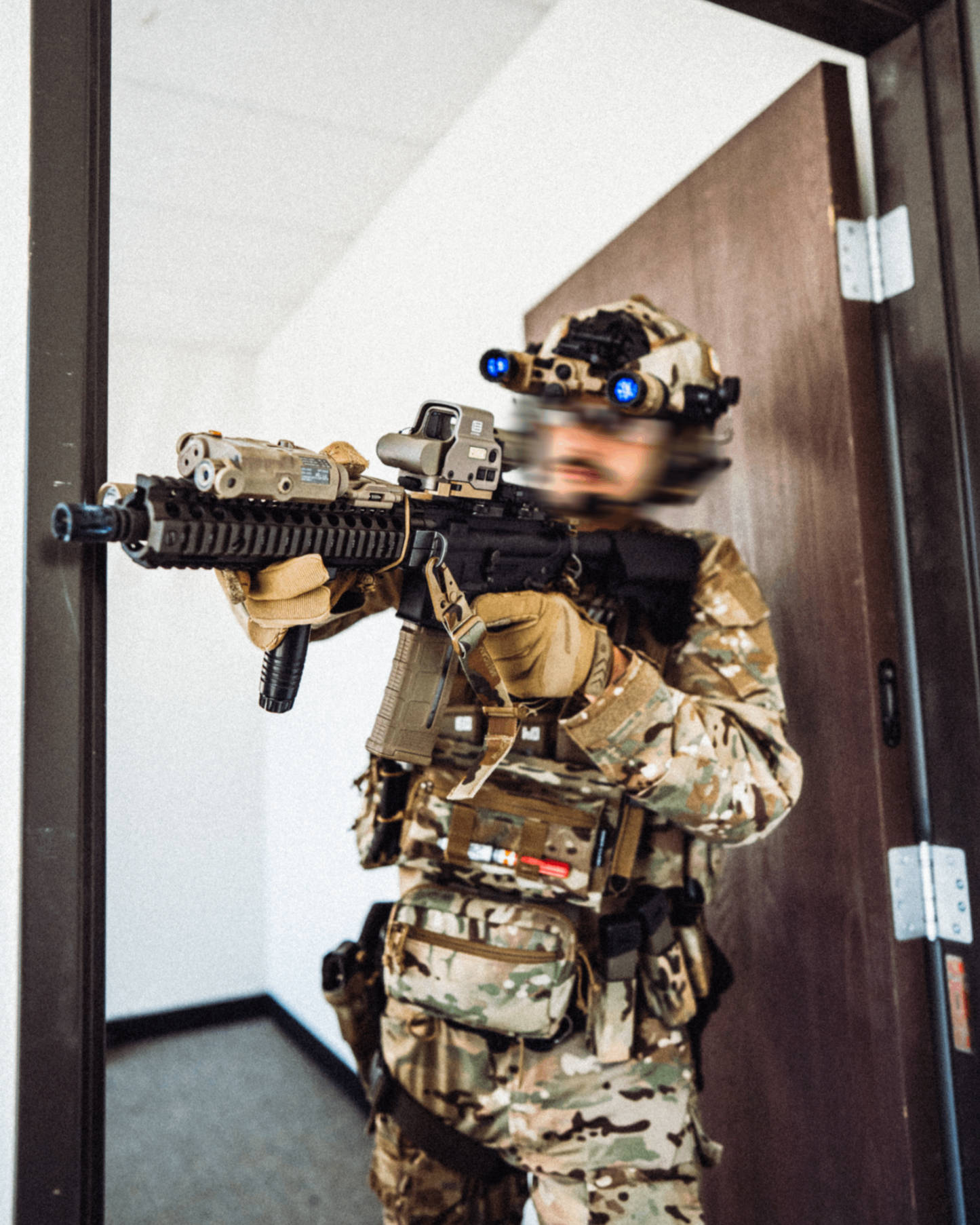 Person in military gear holding a rifle, standing in a doorway.